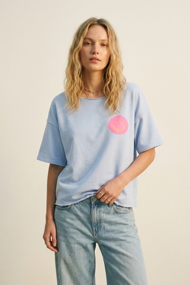 Camiseta azul claro de ajuste holgado con una carita sonriente rosa.