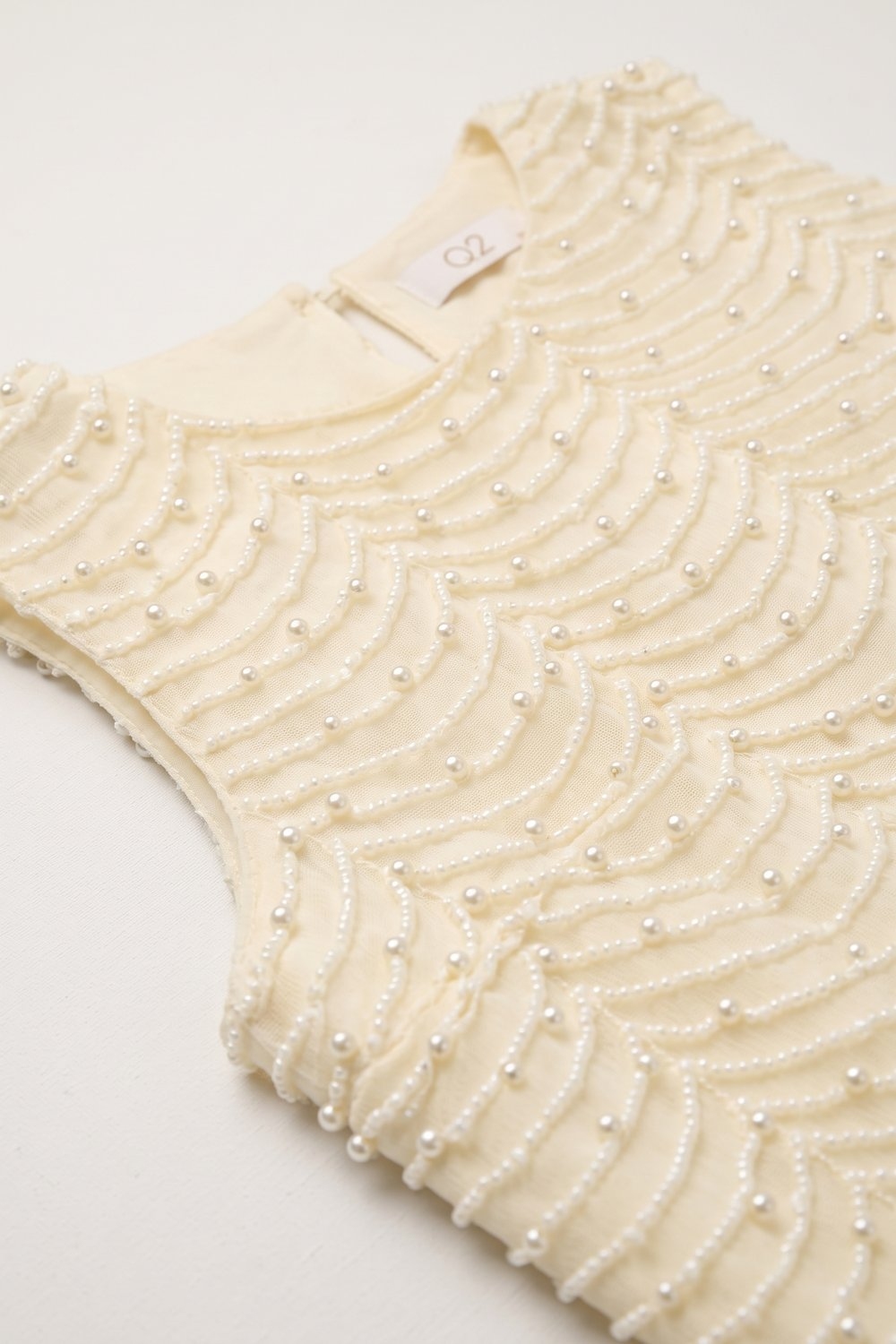 Blusa sin mangas con dobladillo de concha y cuentas adornadas en color crema Blusa sin mangas con dobladillo de concha y cuentas adornadas en color crema